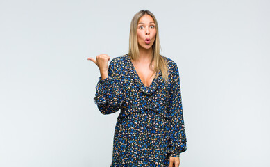 young pretty woman looking astonished in disbelief, pointing at object on the side and saying wow,...