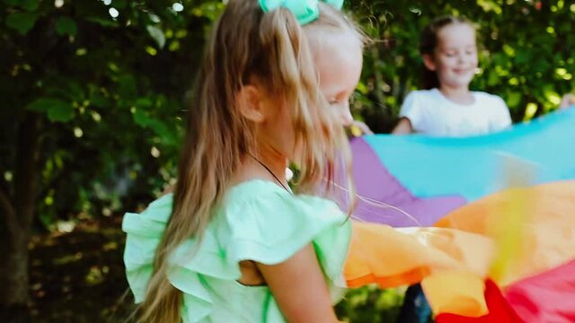 Children playing with colourful toy parachute in the garden. Slow motion video