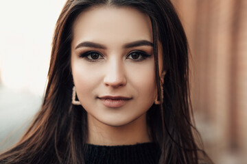 Naklejka premium Close up lifestyle portrait of young indian woman is cold standing on the street cloudy weather, dressed in black pullover and looking at the camera. 