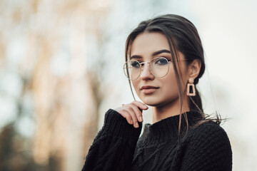 Portrait of young indian woman standing on the street touching her long dark hair, dressed in black...
