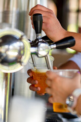 Bartender pouring fresh cold beer from tap into a plastic glass, closeup/Close up on waiter's hands serving beer pints