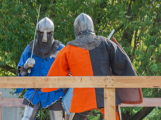 Two knights on foot in heavy medieval armor fight with swords. They are protected by iron helmets...