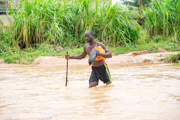 landscape view of african man, walking in a stream, with stick- flood concept