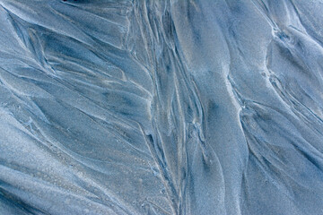 As tide recedes, water creates abstract patterns and textures in beach sand.