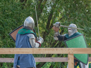 Two knights on foot in heavy medieval armor fight with swords. They are protected by iron helmets...