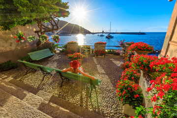 Woman in red with hat in Marciana Marina at sunset sunrays, the flowery old district Borgo al...
