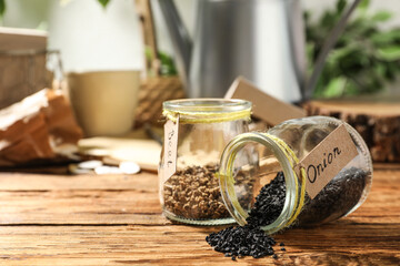 Glass jars with vegetable seeds on wooden table, space for text