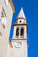 Old city. White stone chapel. Clock on the wall of the chapel. Church tower against the blue sky