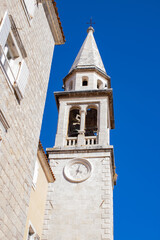 Old city. White stone chapel. Clock on the wall of the chapel. Church tower against the blue sky