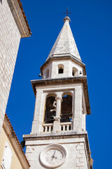 Old city. White stone chapel. Clock on the wall of the chapel. Church tower against the blue sky