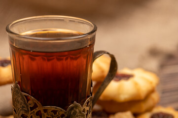 Homemade pastry cookies with jam and a faceted glass of tea in a vintage Cup holder on a background of homespun fabric with a rough texture, close-up, selective focus.