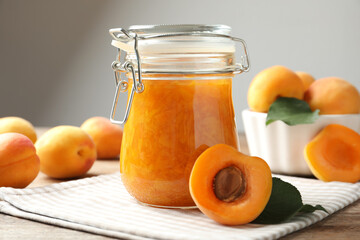 Jar of apricot jam and fresh fruits on table, closeup