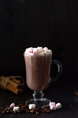 cup of coffee and marshmallows with cinnamon sticks. glass of cappuccino with cream on a dark table. hot chocolate on a wooden background. hot drinks winter and autumn. vertical. copy space.