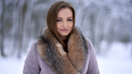 Portrait of a beautiful Russian woman in a coat with fur in the winter forest.