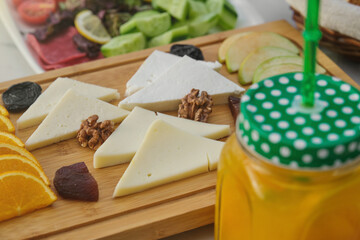 Breakfast table with slices of cheese on a wooden board. Orange juice in jar glass and breakfast foods. Fresh, healthy, light breakfast