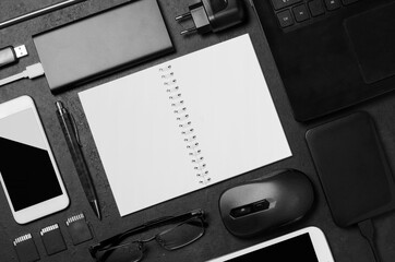 Electronic gadgets and stationery accessories on a black concrete background. Copy space