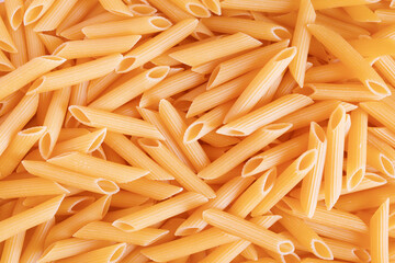 Penne pasta background. Raw organic penne. Traditional Italian penne pasta. Italian Cuisine.  Uncooked dried penne. Top view. Warm tone.