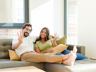 young couple smiling and looking friendly, showing number three or third with hand forward,...