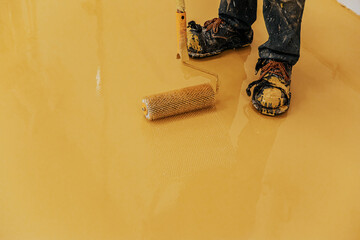 Worker, coating floor with self-leveling epoxy resin in industrial workshop.