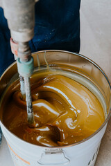Worker mixing yellow epoxy resin with the mixer in a tin bucket