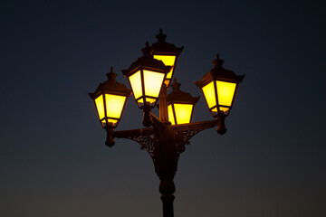 Fototapeta na wymiar Street city cast-iron lantern lit at night, yellow lantern light on dark blue background.