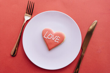 red LOVE cookie on white plate, fork, knife on red table, elegant tableware 
