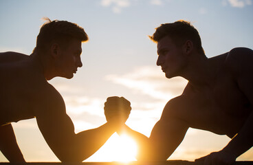 Rivalry, vs, challenge, hand wrestling. Sunset, sunrise. Men measuring forces, arms. Two men arm wrestling. Silhouette of hands that compete in strength. Rivalry, closeup of male arm wrestling