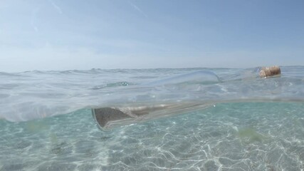 glass bottle with message floats in transparent water of sea or ocean. rolled sheet of paper inside sealed bottle with cork sways on waves against sky.