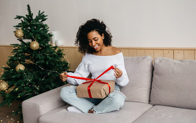 Smiling african american young woman opens box with christmas gift. Christmas lifestyle and...