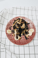 Amazing and easy breakfast, stack of delicious homemade pancakes with chocolate topping, walnuts and sliced bananas