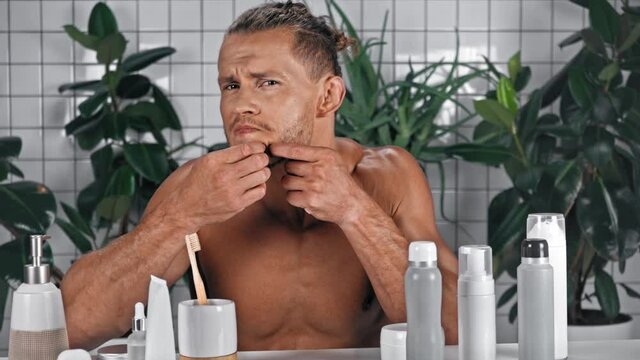 Man looking at camera and squeezing pimple