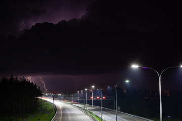 night clouds with lightning over the night track, the track is illuminated by street lights