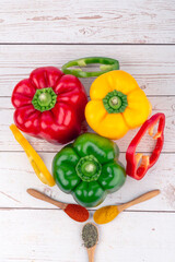 Whole and sliced peppers of different colors accompanied by three wooden spoons with spices,