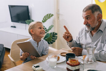 Fototapeta na wymiar grandfather and grandson having breakfast at home, boy using tablet computer