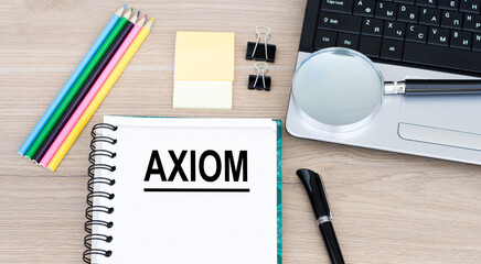 AXIOM word on the notebook on the desktop, next to it is a laptop, pencils, pen, magnifying glass. Business concept