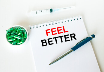 Text Feel Better written in a notebook with a blue pen and a bunch of pills