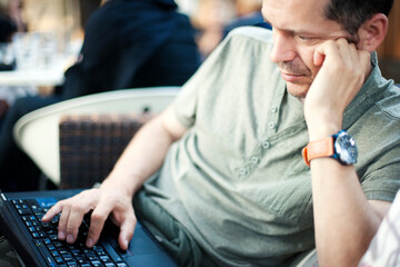 Young man using laptop in cafe outdoors, in soft focus