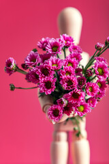 Wooden mannequin is holding bunch of tiny purple flowers like chrysanthemum, concept of giving flower bouquet to lady