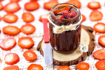 jar of jam with pieces of fruit, made with organic and natural strawberry. Blurred sliced ​​strawberries in the background