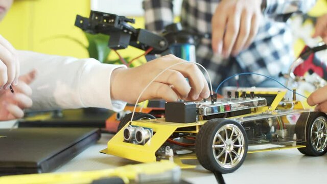 Unrecognizable students assembling car in robotics class