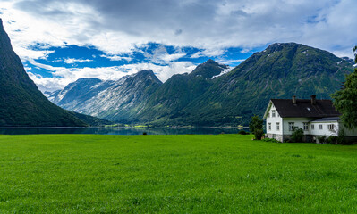 Fototapeta na wymiar Urlaub in Süd-Norwegen: der schöne klare Berg-See Oppstrynsvatnet mit Haus und saftiger Wiese / Segestad