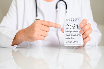 Arzt mit einem Notizblock und Vorsätzen für 2021 weniger Alkohol und Rauchen, weniger Stress,...