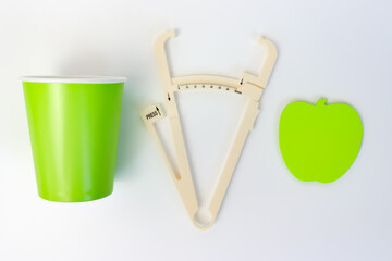 A glass of water, caliper and apple shaped sticky notes on white background, weightloss and dieting...