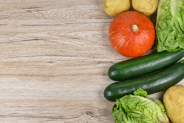 Helathy raw Hokkaido squash, zucchini, lettuce and potatoes on side of wooden background with empty copy space