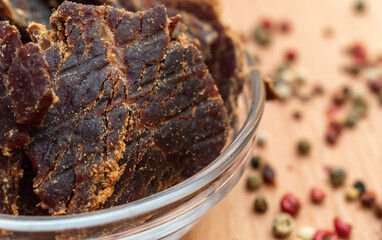 Bowl with beef jerky and spices on wooden background.