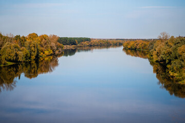 A wide river with an autumn landscape against a blue sky.