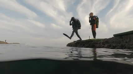 scuba diver in diving suit is jumping into water from seashore. 