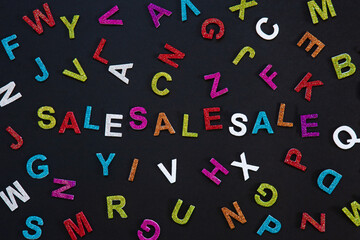 Sale label on a black background surrounded by colorful letters of the alphabet