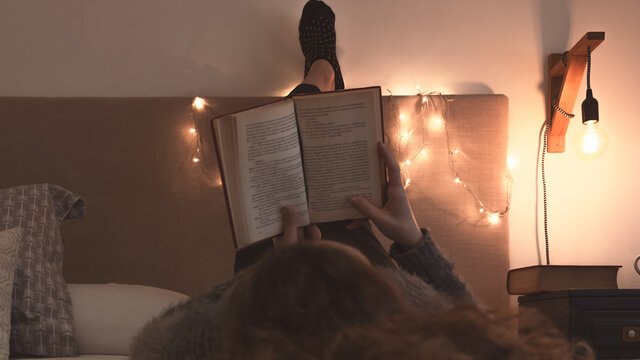 Tiempo de relajarse y disfrutar de un buen libro desde la comodidad del hogar. Retrato de mujer joven adulta recostada leyendo sobre la cama en una agradable y c&aacute;lida habitaci&oacute;n en una tarde oto&ntilde;al. 
