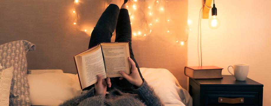 Tiempo de relajarse y disfrutar de un buen libro desde la comodidad del hogar. Retrato de mujer joven adulta recostada leyendo sobre la cama en una agradable y c&aacute;lida habitaci&oacute;n en una tarde oto&ntilde;al. 